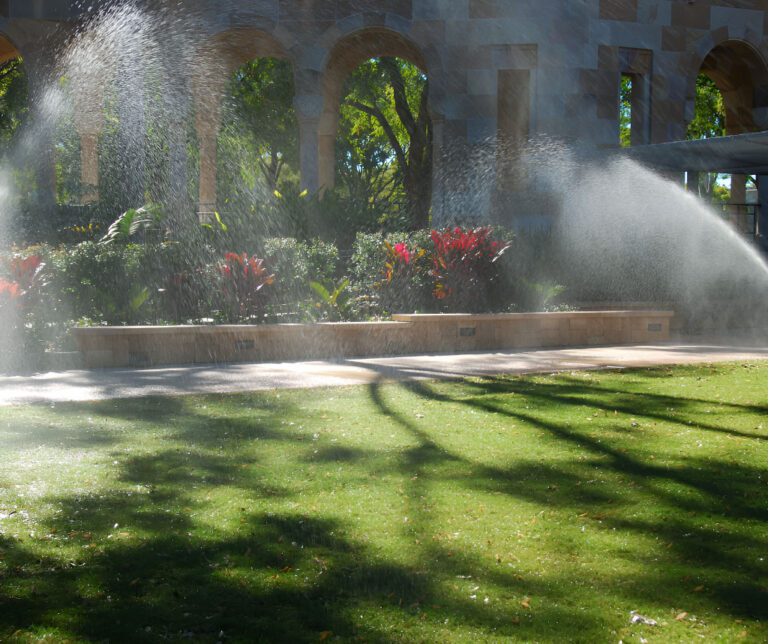 Sunlit garden with spraying water and arched structure.