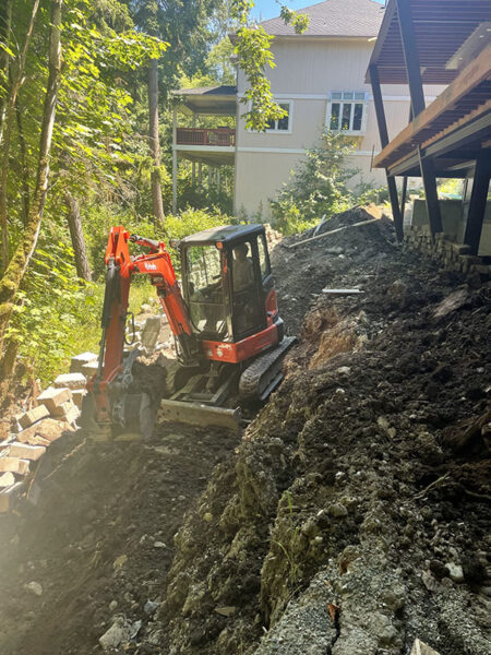 Mini excavator on rocky terrain near residential building